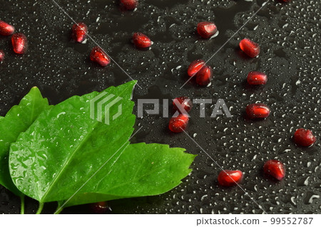 Closeup juicy fresh pomegranate arils with green leaf on black Closeup juicy fresh pomegranate arils with green leaf on black 99552787