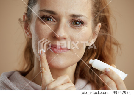 40 years old woman applying ointment using finger against beige 40 years old woman applying ointment using finger against beige 99552954