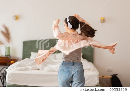 Happy young Caucasian woman wearing headphones spinning dance and enjoy life. Back view. Leisure in home Happy young Caucasian woman wearing headphones spinning dance and enjoy life. Back view. Leisure in home 99553339