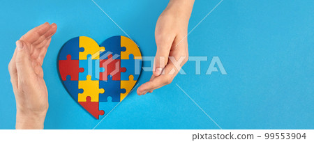 Father and autistic son hands holding jigsaw puzzle heart shape. World Autism Awareness Day 99553904