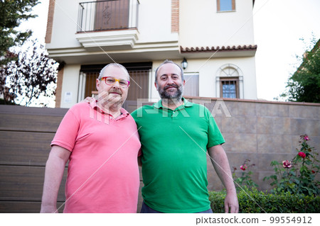 Happy middle-aged male couple smiling with their new house Happy middle-aged male couple smiling with their new house 99554912