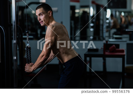 Shirtless man doing triceps pulldown at the gym.  99556376