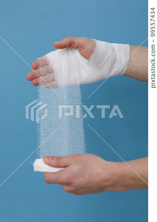 Concept of help during an injury, man wrapping hand in bandage on blue background 99557434