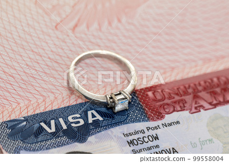 Ring with a diamond on the background of a US visa as a symbol of engagement 99558004