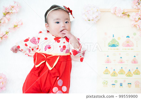 A cute girl baby in a red hakama who looks happy surrounded by spring cherry blossoms at the Hinamatsuri of the first festival 99559900