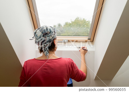 Woman paints a window recess of a roof window with a brush - painting concept 99560035
