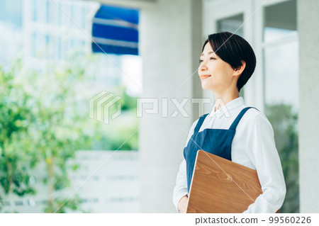 Middle-aged woman welcoming customers in front of a cafe Middle-aged woman welcoming customers in front of a cafe 99560226