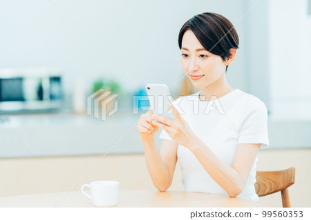 一位在廚房裡操作智能手機的中年婦女。 99560353