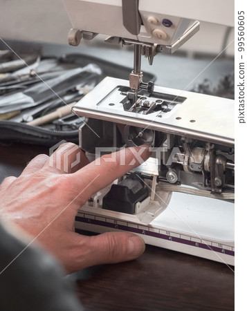 Finger of the sewing machine adjuster repairs the internal mechanism. Professional adjustment of a sewing machine in a small factory. Cleaning and repair of professional equipment. Vertical view Finger of the sewing machine adjuster repairs the internal mechanism. Professional adjustment of a sewing machine in a small factory. Cleaning and repair of professional equipment. Vertical view 99560605