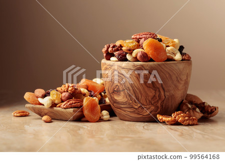 Dried fruits and nuts on a beige ceramic table. 99564168