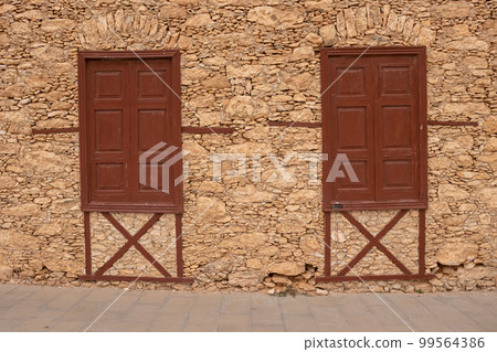 Stones wall and two windows with closed shutters Stones wall and two windows with closed shutters 99564386