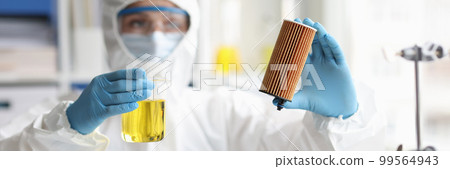 Scientist in protective suit holds car filter cartridge in laboratory and oil 99564943