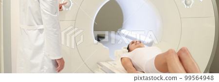 In medical laboratory male radiologist controls MRI or CT scan with female patient 99564948