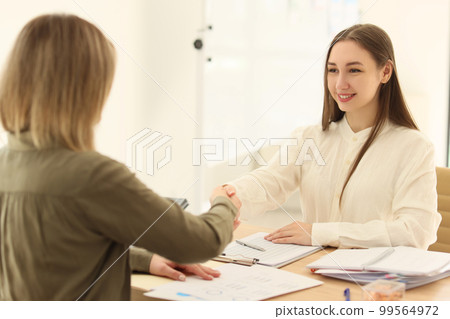 Young women in the office at the table shake hands Young women in the office at the table shake hands 99564972