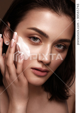 Beautiful young girl with natural nude make-up with cosmetics cream in hands. Beauty face. Beautiful young girl with natural nude make-up with cosmetics cream in hands. Beauty face. 99565748