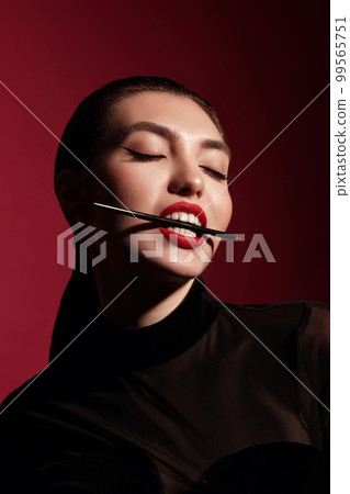 Beautiful woman in black clothes, classic make-up and red lips posing in the studio on a red background. Beautiful woman in black clothes, classic make-up and red lips posing in the studio on a red background. 99565751