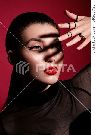 Beautiful woman in black clothes, classic make-up and red lips posing in the studio on a red background. Beautiful woman in black clothes, classic make-up and red lips posing in the studio on a red background. 99565753