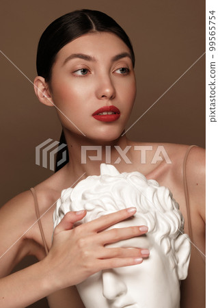 A beautiful woman with classic make-up, red lips and a plaster male bust in her hands. Beauty face A beautiful woman with classic make-up, red lips and a plaster male bust in her hands. Beauty face 99565754