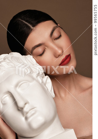 A beautiful woman with classic make-up, red lips and a plaster male bust in her hands. Beauty face A beautiful woman with classic make-up, red lips and a plaster male bust in her hands. Beauty face 99565755