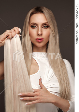 Beautiful blond girl with a perfectly hair, and classic make-up with a strand of hair for extension. Beauty face and hair. 99565759