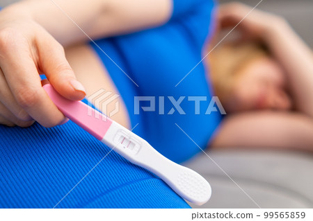 Upset young woman with a positive pregnancy test laying down on the sofa. Upset young woman with a positive pregnancy test laying down on the sofa. 99565859