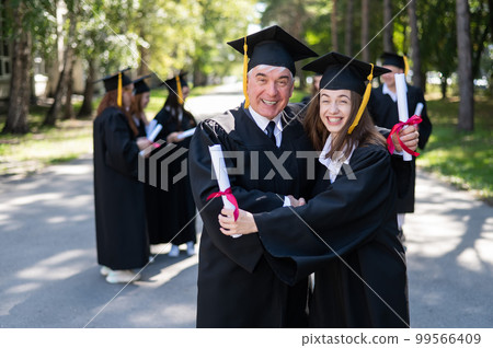A group of graduates in robes outdoors. An elderly man and a young woman congratulate each other on their graduation. A group of graduates in robes outdoors. An elderly man and a young woman congratulate each other on their graduation. 99566409