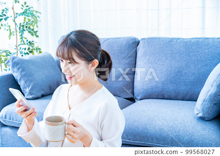 A woman who uses a smartphone while drinking coffee A woman who uses a smartphone while drinking coffee 99568027