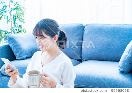 A woman who uses a smartphone while drinking coffee 99568028