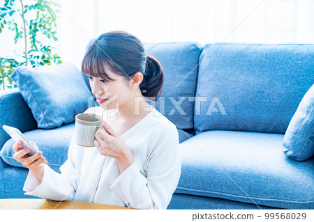 A woman who uses a smartphone while drinking coffee 99568029