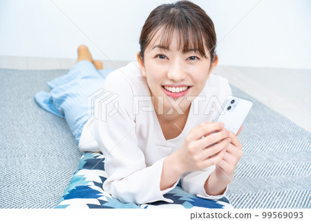 Woman who lays down and uses smartphone 99569093