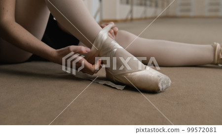 Female ballet dancer takes off pointe shoes 99572081