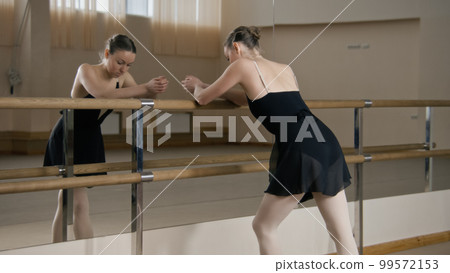 Tired ballerina stands near ballet barre 99572153