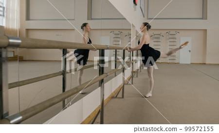 Ballerina stretches legs near ballet barre 99572155