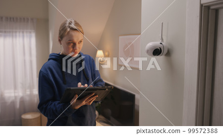 Woman sets up angle of CCTV camera at home Woman sets up angle of CCTV camera at home 99572388