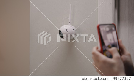 Woman sets up angle of CCTV camera with phone Woman sets up angle of CCTV camera with phone 99572397