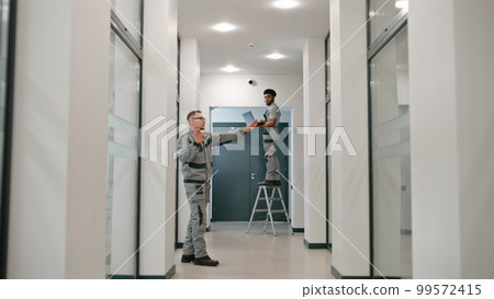 Two multi ethnic installers in uniform sets up security camera 99572415