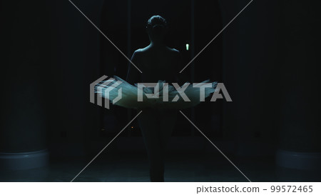 Ballerina rehearses in dark theater lobby at night 99572465