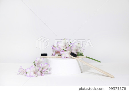Creative representation of dentistry and oral care products. Bamboo toothbrushes on a podium pedestal with plant, flowers, on a white gray table background. Dental care Creative representation of dentistry and oral care products. Bamboo toothbrushes on a podium pedestal with plant, flowers, on a white gray table background. Dental care 99575876