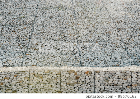 Granite stones behind a metal grate for strengthening the slope. Stones behind the wire. grey texture. construction. 99576162