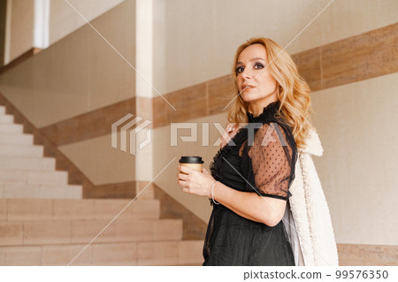 Portrait of a beautiful smiling blonde. She's walking up the stairs, coffee in hand. The Concept Of Urban Life. 99576350