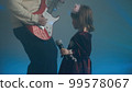 Little girl on stage in vintage dress, she sings into microphone and dances, her father plays an electric guitar. Color music is shining and smoke is billowing. Family time, creativity and hobbies 99578067