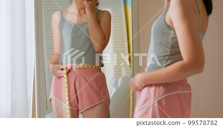 unhappy woman measure her waist 99578782