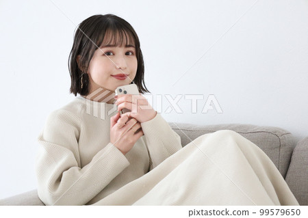 一個女人坐在沙發上，拿著智能手機微笑 99579650