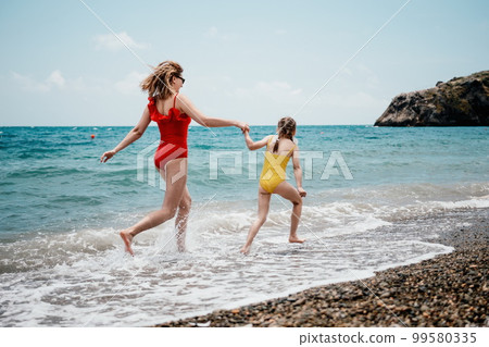Happy loving family mother and daughter having fun together on the beach. Mum playing with her kid in holiday vacation next to the ocean - Family lifestyle and love concept Happy loving family mother and daughter having fun together on the beach. Mum playing with her kid in holiday vacation next to the ocean - Family lifestyle and love concept 99580335