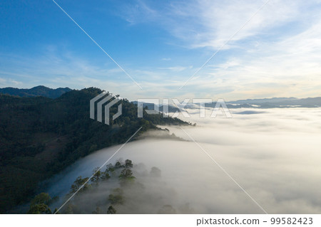 aerial view scenery sunrise above the mountain in tropical rainforest. slow floating fog blowing cover on the mountain look like as a sea of mist. beautiful sunrise in the mist background. aerial view scenery sunrise above the mountain in tropical rainforest. slow floating fog blowing cover on the mountain look like as a sea of mist. beautiful sunrise in the mist background. 99582423