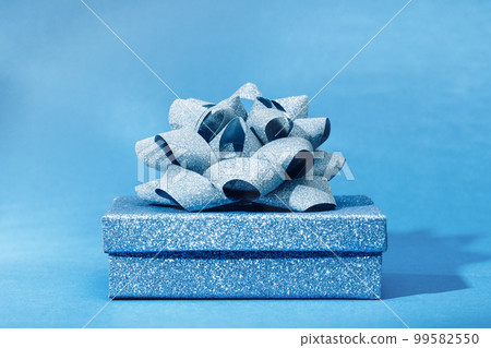 Luxury gift glitter box with a blue bow on blue. Side view monochrome. Fathers day or Valentines day gift for him. Baby shower or gender reveal birthday party. Festive sale 99582550