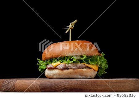 burger with a latch on a wooden board on a black background burger with a latch on a wooden board on a black background 99582836