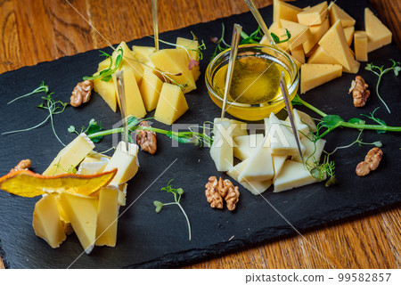 different types of cheese on a black board with honey and nuts 99582857