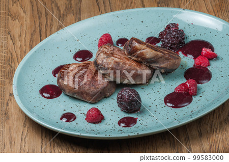 Three small baked steaks on a plate with sauce and raspberries 99583000