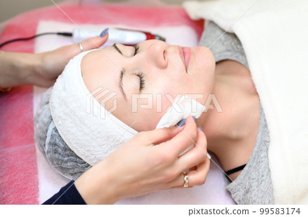 A woman cosmetologist washes a client with cotton wool and water, 99583174